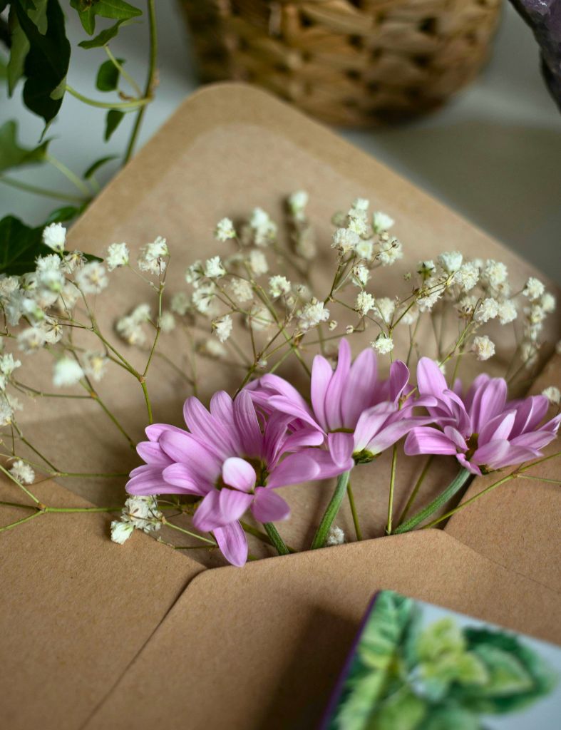 flowers peeking out of a brown paper envelope placed on a desk, with soft greens and wicker in the background